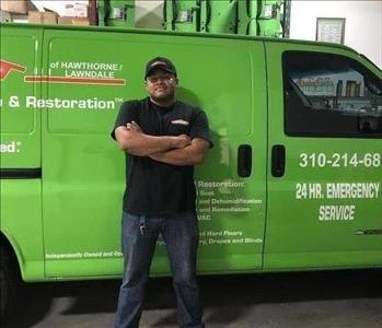 Male employee in a black hat and shirt in front of a green SERVPRO van